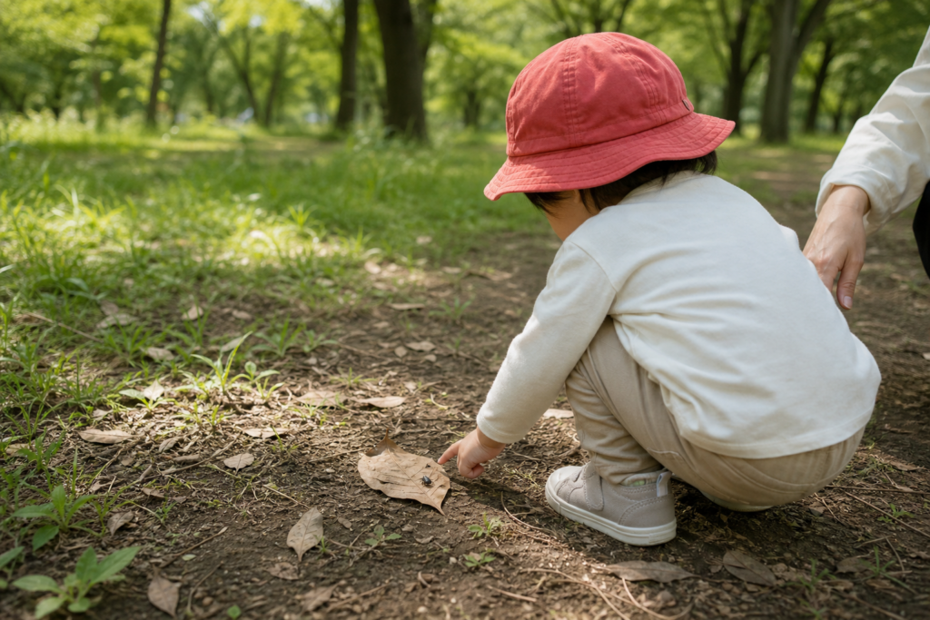 公園の土の上で落ち葉と小さな虫を見つめる子どものイメージ